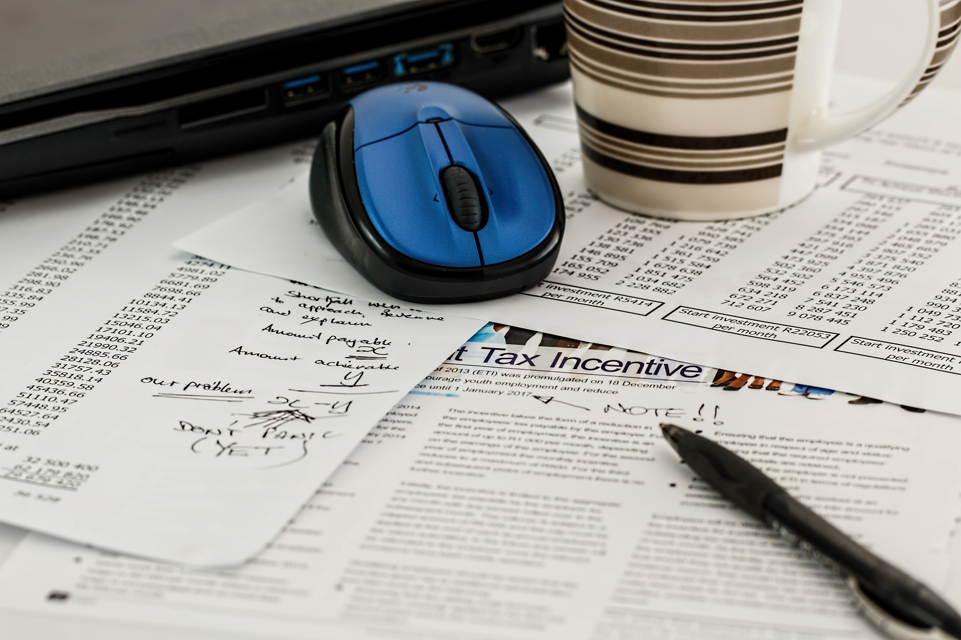 laptop with mouse and a cup on top of report papers